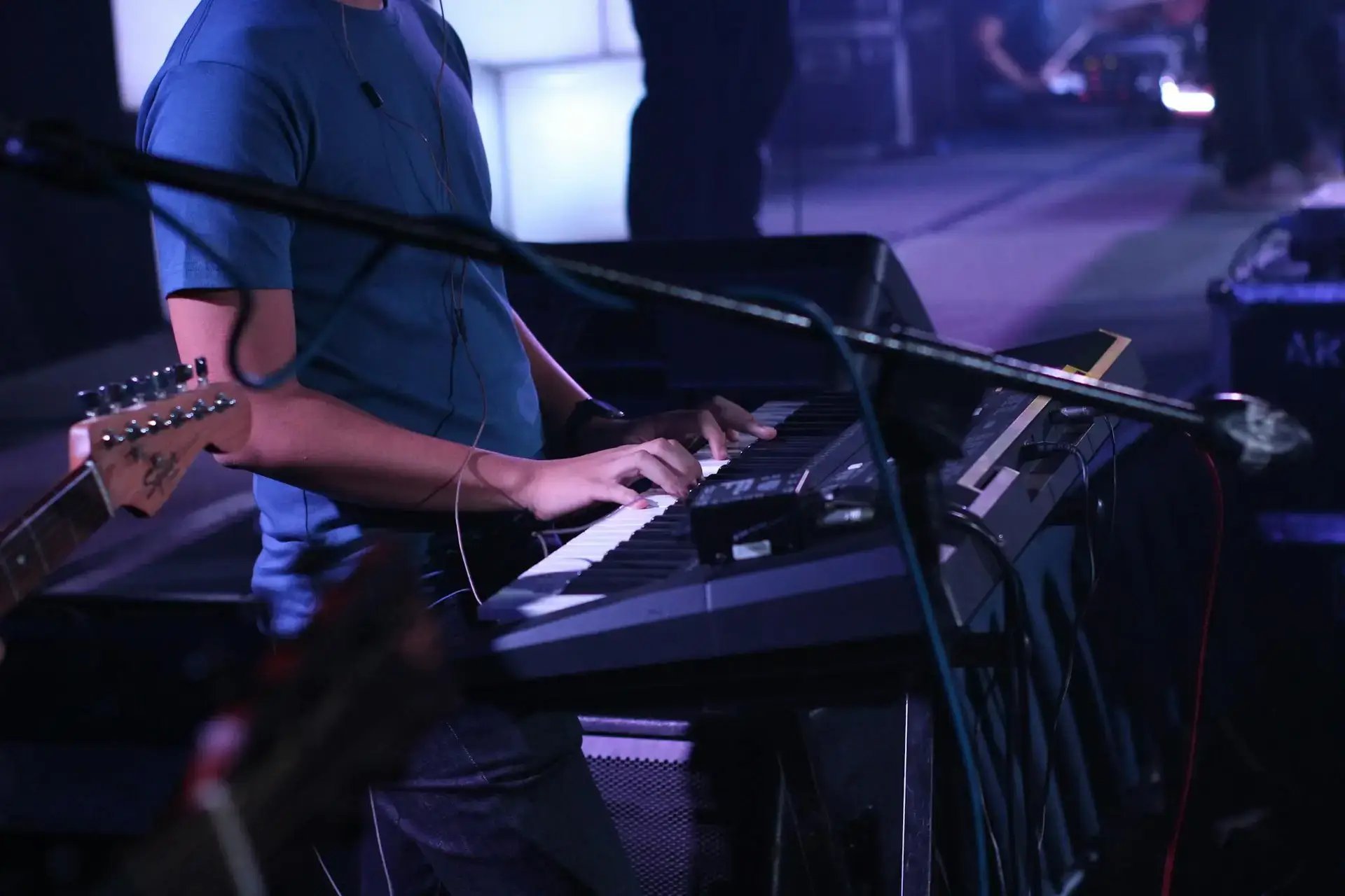 A musician performs on a keyboard during a dynamic live concert, surrounded by instruments.